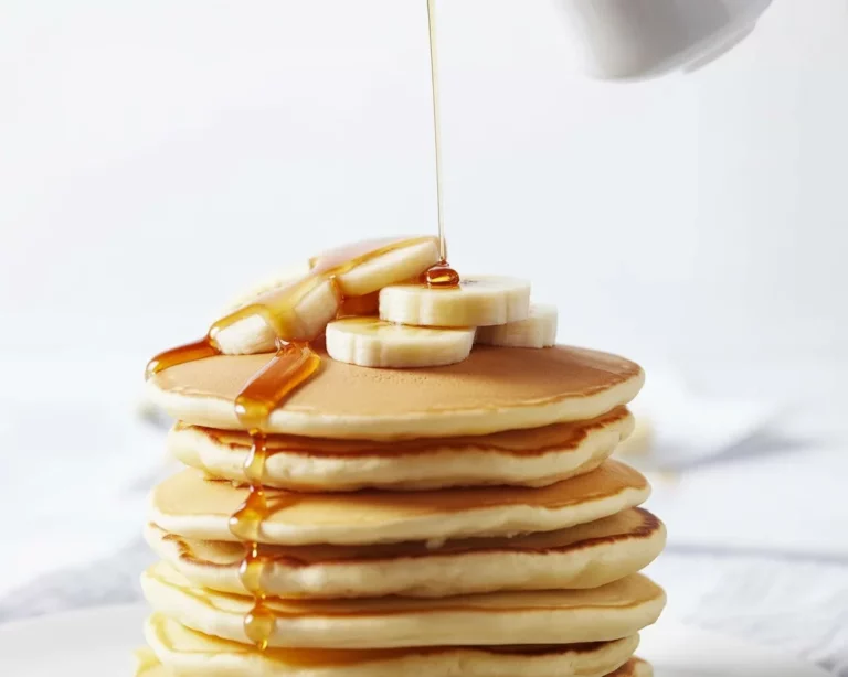 Ein Teller mit fluffigen veganen Pfannkuchen, serviert mit frischen Früchten und Ahornsirup.
